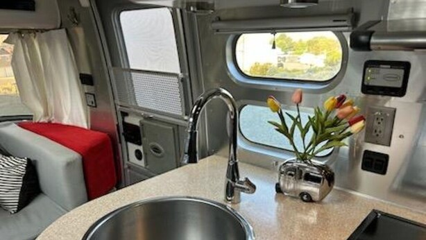 A kitchenette with a stainless steel sink, a small countertop, and a window with a view. - Classic Airstream (Quincy)