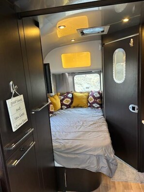 A compact RV interior with a bed, a small window, and a door with a sign.