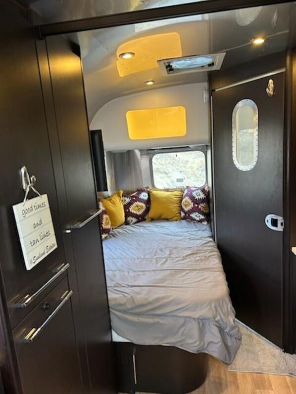A compact RV interior with a bed, a small window, and a door with a sign.