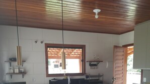 A kitchen with a wooden countertop, a stool, and a window with a view of the outside. - Sítio Martinelli, your connection with Nature, come and have a well-deserved rest. (São Lourenço Santa Teresa)