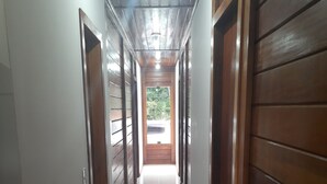A hallway with wooden paneling and a tiled floor, leading to a bright area with a view of greenery outside. - Sítio Martinelli, your connection with Nature, come and have a well-deserved rest. (São Lourenço Santa Teresa)