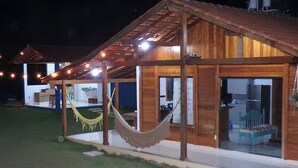 A wooden cabin with a covered porch, a hammock, and a small garden area. - Sítio Martinelli, your connection with Nature, come and have a well-deserved rest. (São Lourenço Santa Teresa)