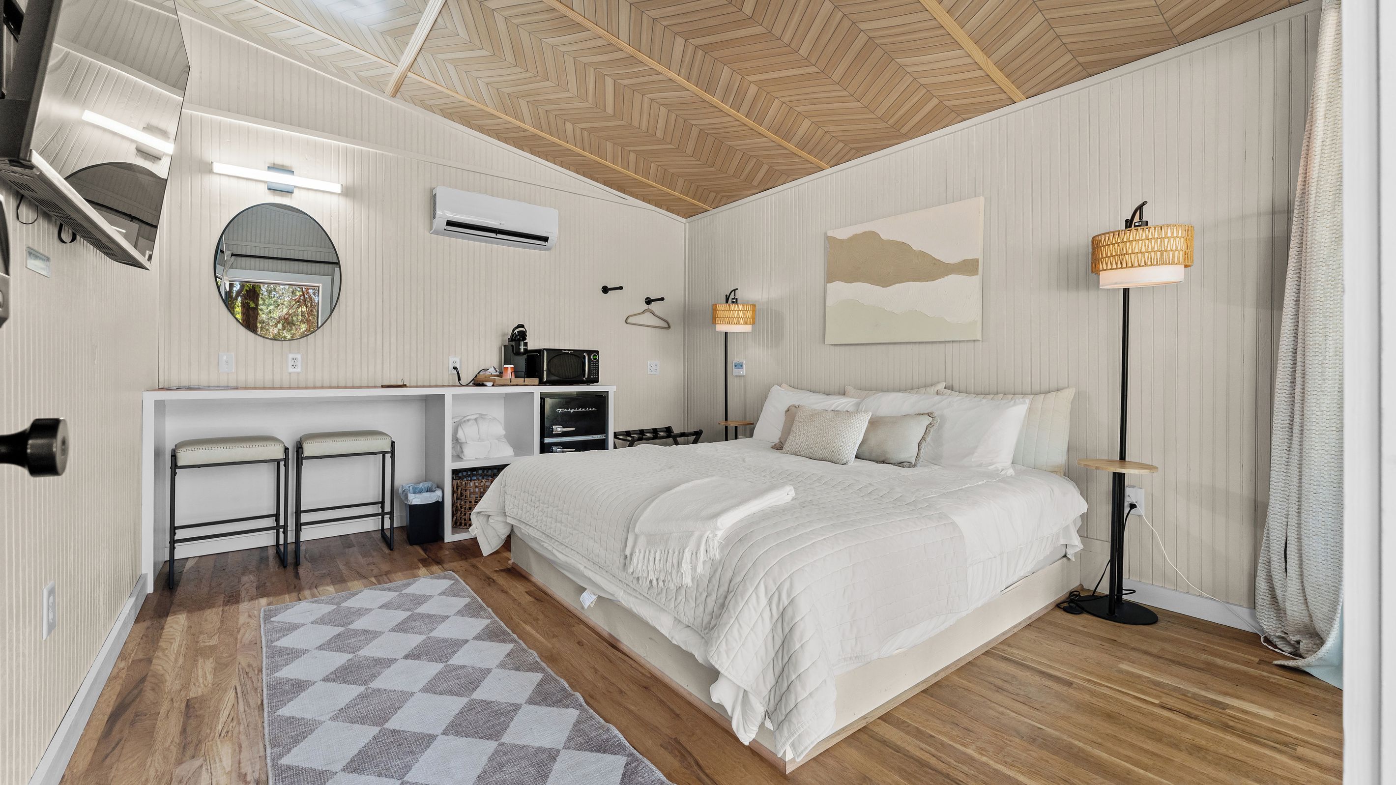 Ein Hotelzimmer mit einem Bett, einem Schreibtisch mit Stuhl, einer Mikrowelle, einer Hängelampe und Blick ins Freie.