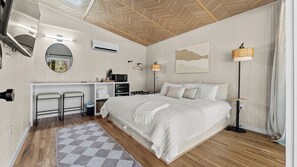 Quarto de hotel com cama, escrivaninha e cadeira, micro-ondas, luminária pendente e vista para o exterior.
