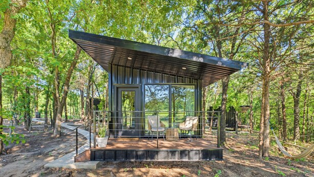 A modern wooden cabin with large windows, a deck, and outdoor seating. - The Red Bird | Treehouse Stay + Pickleball Court (Alvord)