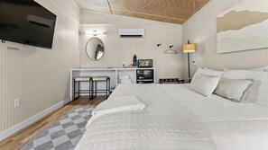 A hotel room with a large bed, a desk with two chairs, a flat-screen TV, a microwave, and a small kitchenette. - The Red Bird | Treehouse Stay + Pickleball Court (Alvord)
