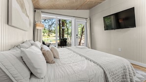 Een slaapkamer met een groot bed, een aan de muur bevestigde televisie en uitzicht op een buitenruimte met een tafel en stoelen.