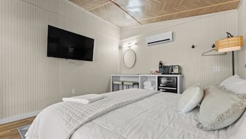 A hotel room with a bed, a TV, a minibar, and a wall-mounted air conditioner.