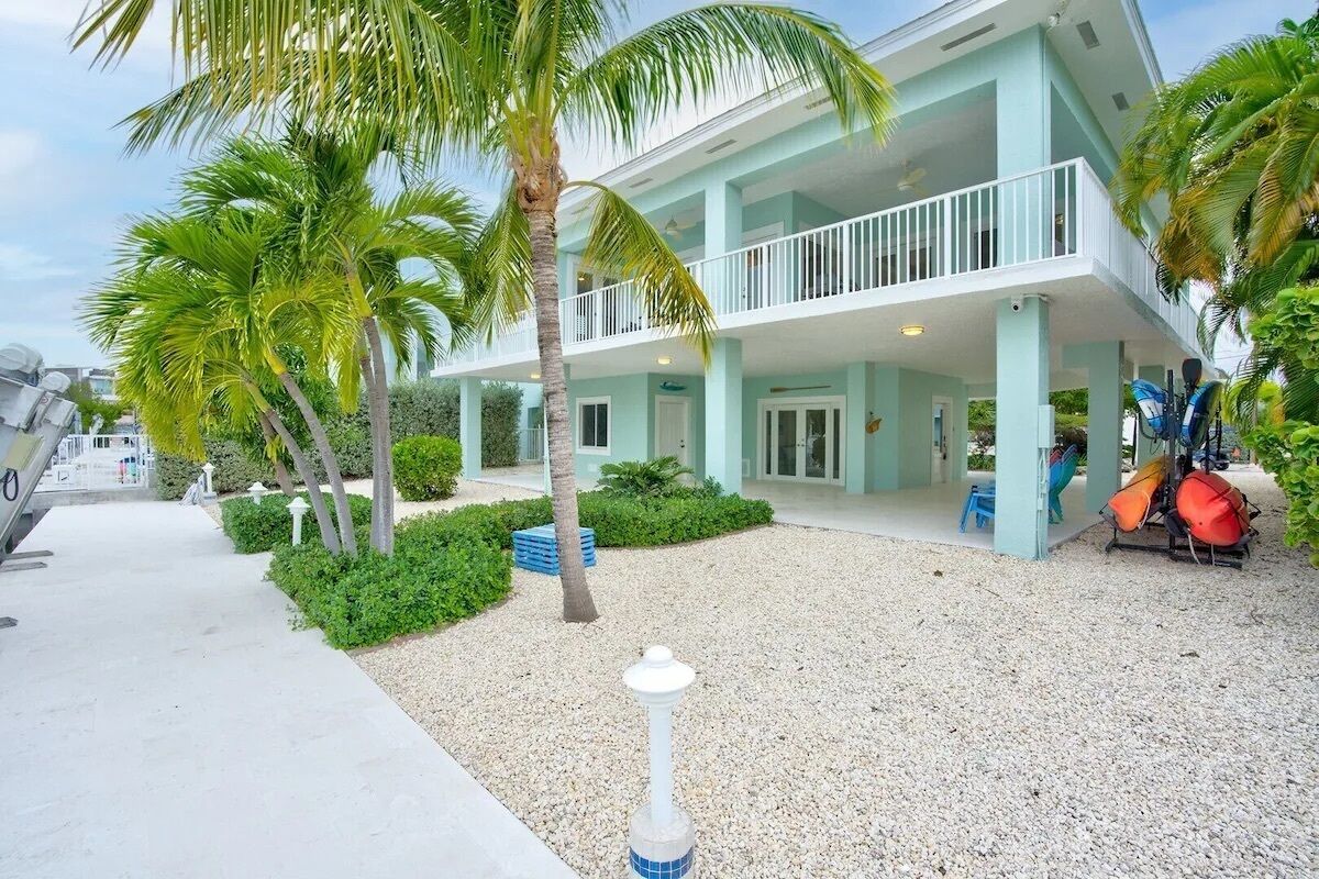 A two-story building with a light blue exterior, a balcony on the upper floor, and a gravel driveway.