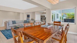A spacious living area with a large wooden dining table, comfortable seating, and a modern chandelier.