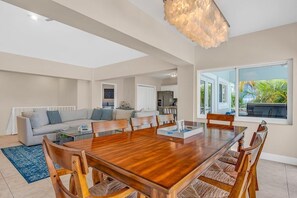 Uma sala de estar ampla com uma grande mesa de jantar de madeira, assentos confortáveis e um lustre moderno.