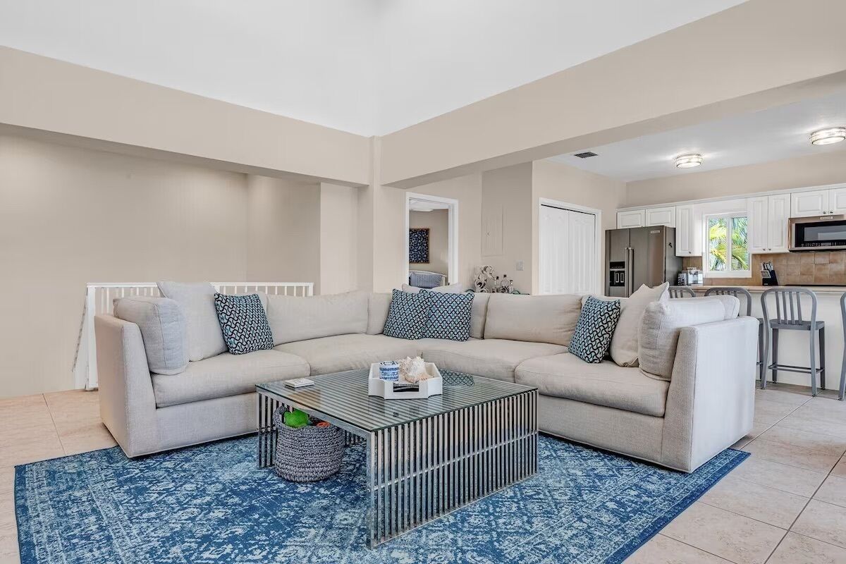 A modern living room with a beige sectional sofa, a glass coffee table, and a blue patterned rug.