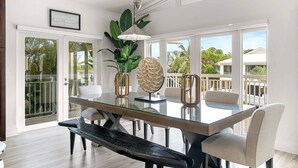 A modern dining area with a glass table, white chairs, and a view of the outdoors.