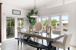 Uma área de jantar moderna com mesa de vidro, cadeiras brancas e vista para o exterior.