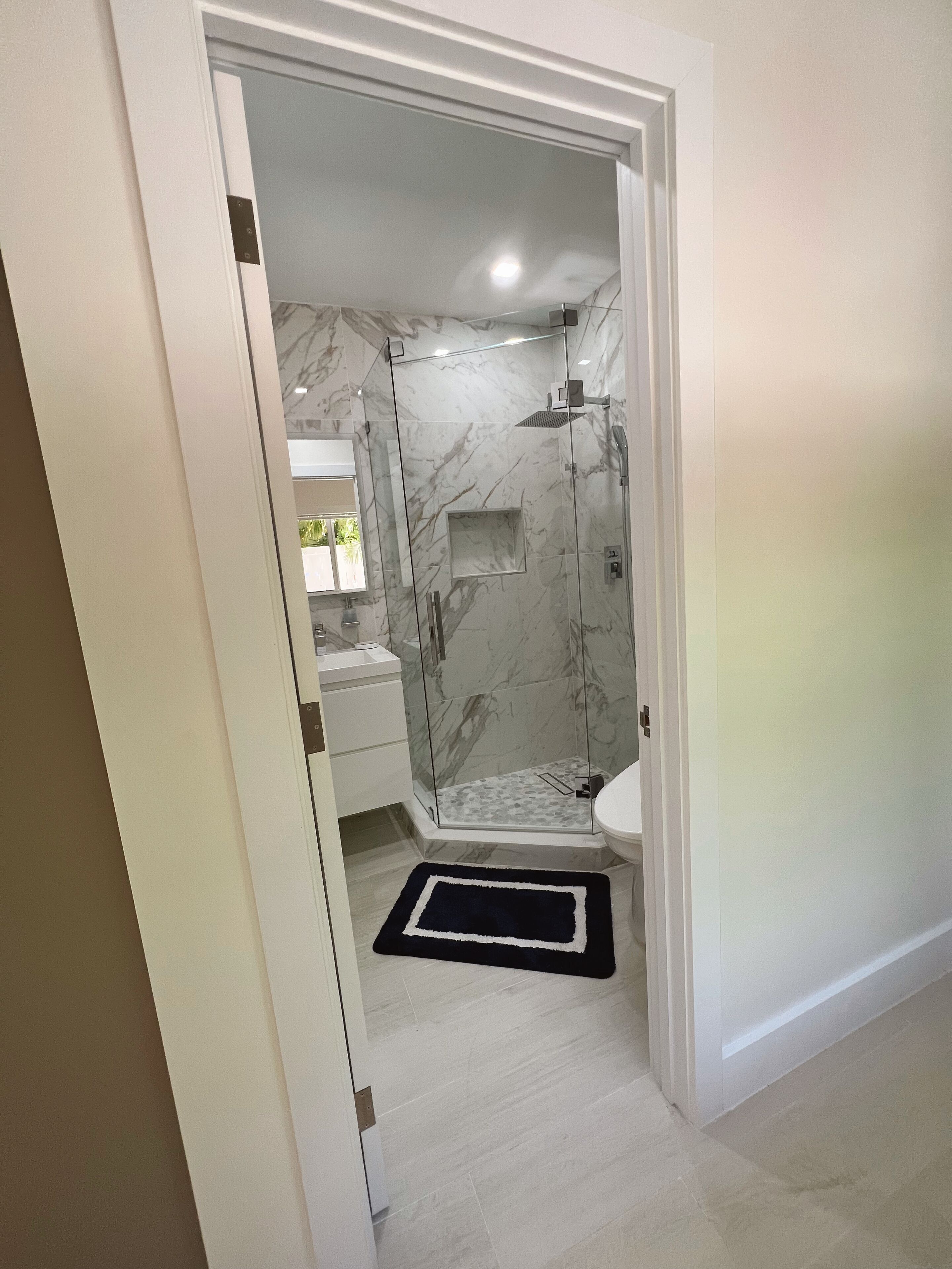 A modern bathroom with a glass-enclosed shower, marble walls, and a white sink.