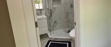 A modern bathroom with a glass-enclosed shower, marble walls, and a white sink.