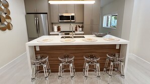 A modern kitchen with a central island, stainless steel appliances, and clear glass bar stools.