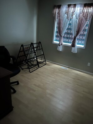 A room with a wooden floor, a black office chair, and a black metal shelf unit. - Enjoy a rural 2 bedroom 2 bath family home with garage in north west Manitoba. (Mafeking)