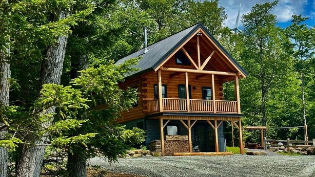 Une cabane en bois dotée d’un balcon, entourée d’arbres et bordée d’une allée de gravier.
