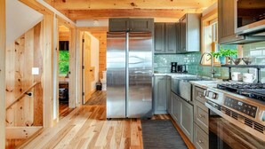 A modern kitchen with wooden floors, stainless steel appliances, and grey cabinets. - The Greylock Cabin (Florida)