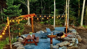Un espace extérieur aménagé avec une table et des chaises en bois, un petit foyer et des guirlandes lumineuses.