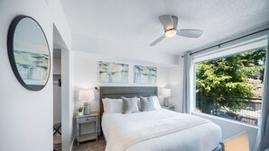 Un hotel moderno con una cama grande, dos mesitas de noche con lámparas, un ventilador de techo y obras de arte en las paredes.
