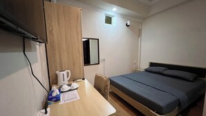 A bedroom with a bed, a desk, a mirror, and a small window.