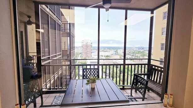 A balcony with a table, chairs, a potted plant, and a view of a cityscape.