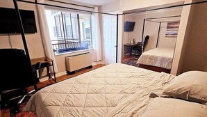 A hotel room with a large bed, a desk, a chair, and a TV.
