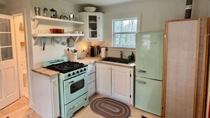 Cocina compacta con muebles blancos, estufa y refrigerador.