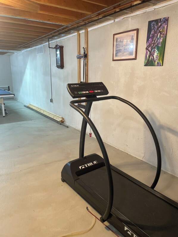 Una cinta de correr en una habitación con mesa de ping pong, un cuadro enmarco y un cuadro colgado en la pared.