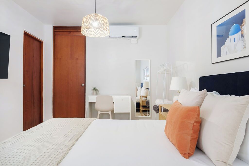 A hotel room with a bed, a desk, a chair, a wardrobe, and a hanging light fixture.