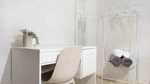 Un baño minimalista con un escritorio blanco, una silla y un perchero con toallas enrolladas.