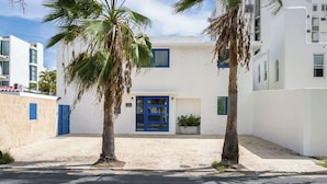 Un edificio con puerta y ventanas azules, rodeado de palmeras y suelo arenoso.