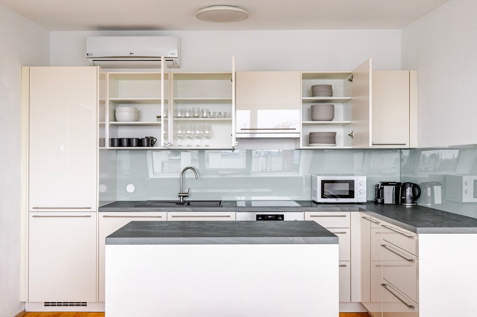 A modern kitchen with white cabinets, a built-in microwave, a sink, and a coffee maker.