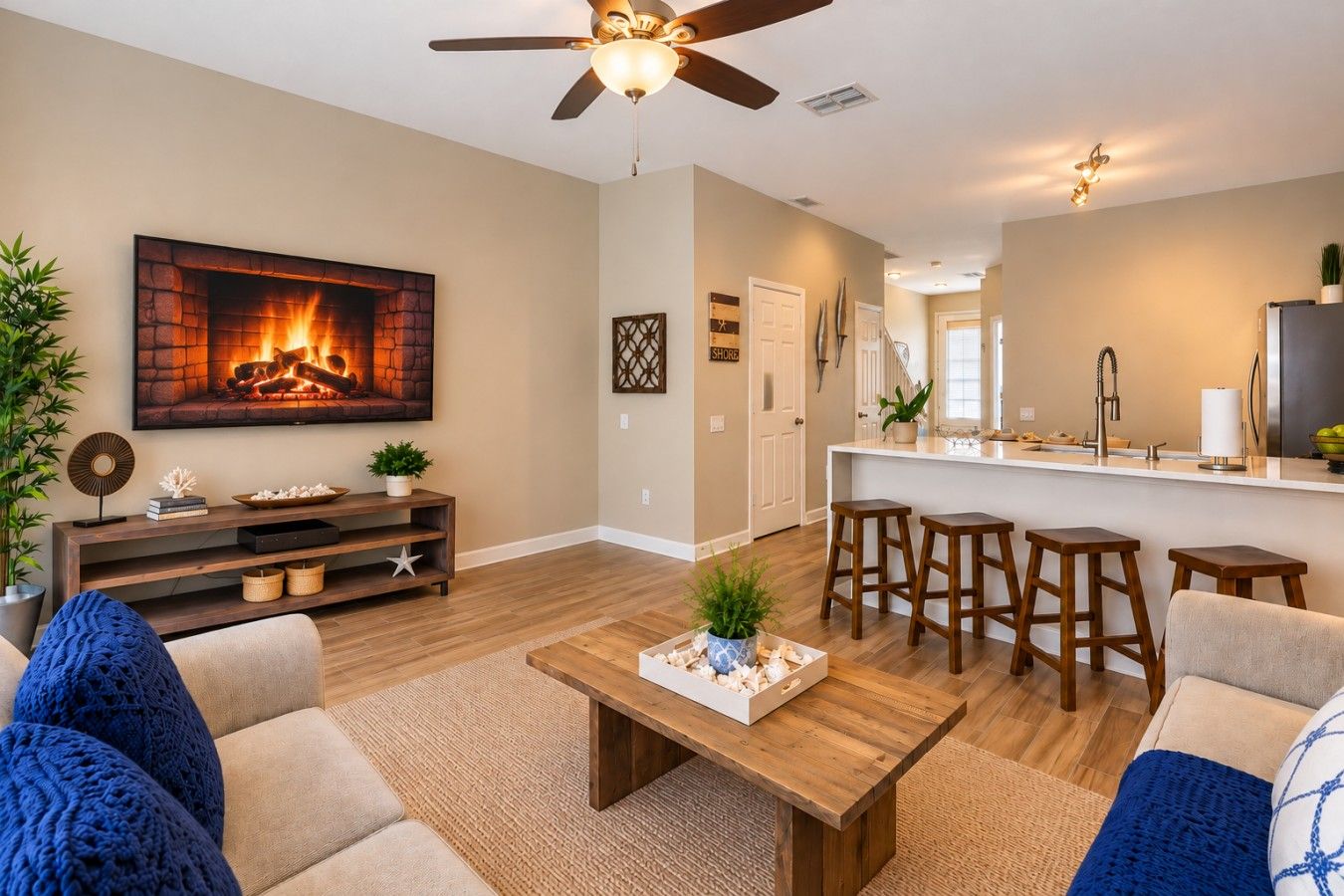 A modern living room with a fireplace, a ceiling fan, and a kitchen area with bar stools.