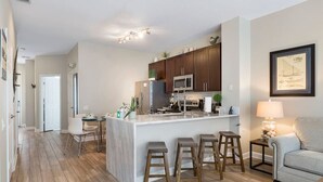 A modern kitchen with a central island, wooden stools, and a dining area with chairs. - Amazing 3BDR House w/ pool (Kissimmee)