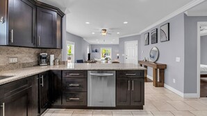A modern kitchen with dark cabinetry, a granite countertop, and a built-in dishwasher.