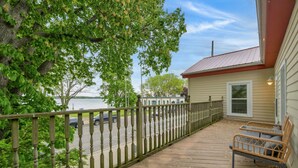 A wooden deck with a railing, a bench, and a view of a road and parked cars. - Lighthouse Loft– Chic Getaway in Marine City (Marine City)
