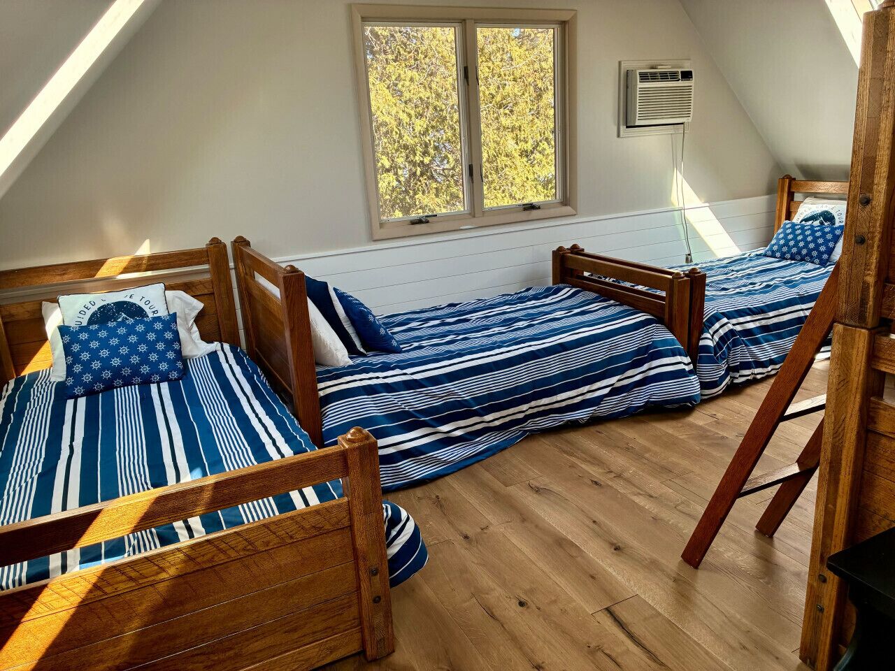 A dormitory room with three wooden beds, a skylight, and a window with an air conditioning unit.