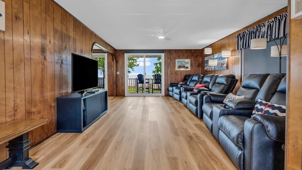 A modern living room with a wooden interior, a flat-screen TV, leather sofas, and a sliding glass door leading to an outdoor area. - Knot a Care - Lakefront Living with Great Views! (Port Hope)