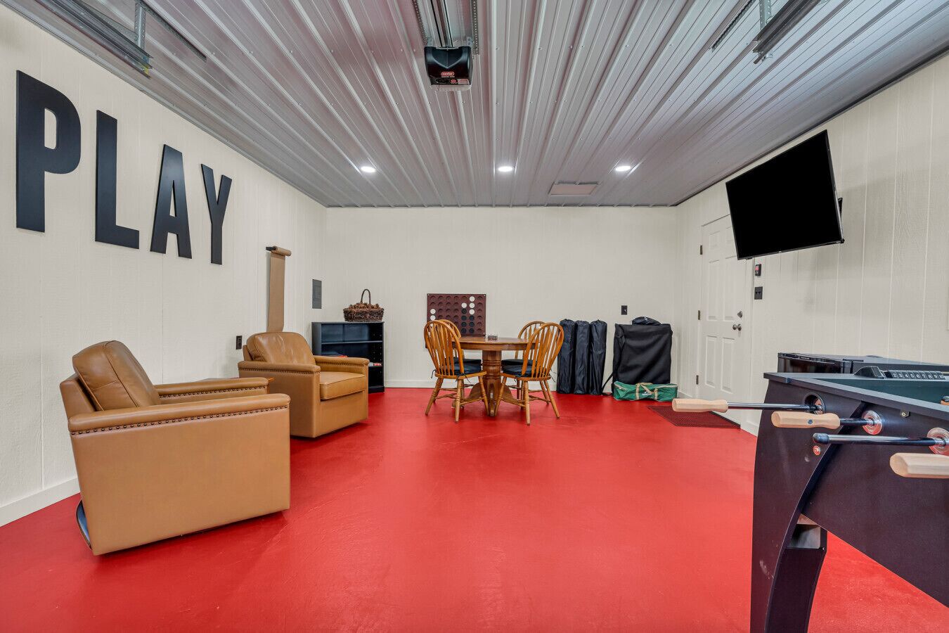 Ein Zimmer mit rotem Boden, einem Billardtisch, einer Couch, einem Fernseher und einer Wand mit der Aufschrift 'PLAY'.