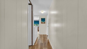 A hallway with white walls and wooden flooring leading to a kitchen area with a blue countertop and a painting on the wall. - Knot a Care - Lakefront Living with Great Views! (Port Hope)