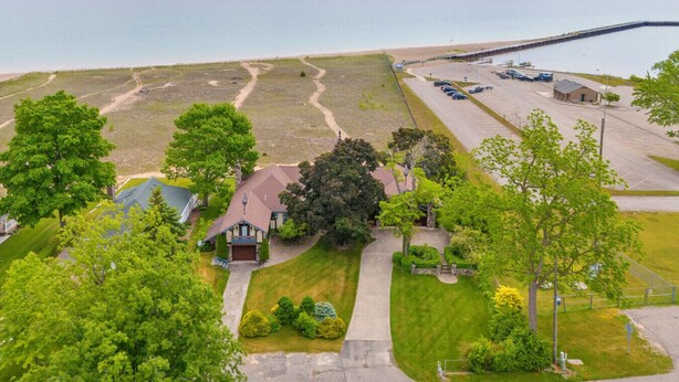 A coastal property with a large lawn, a house with a red roof, and a parking area with cars. - Steps to the Sand! Ultimate Beach House Get-A-Way! (Port Sanilac)