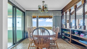 A dining area with a round table and chairs, large windows with curtains, and a view of the beach. - Steps to the Sand! Ultimate Beach House Get-A-Way! (Port Sanilac)