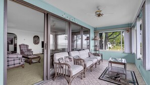 A spacious room with a sliding glass door leading to a balcony, a sofa set, a coffee table, and a ceiling fan. - Steps to the Sand! Ultimate Beach House Get-A-Way! (Port Sanilac)
