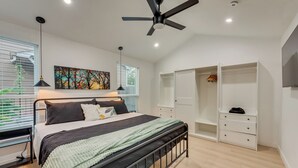 A modern bedroom with a bed, ceiling fan, wardrobe, and artwork on the wall.