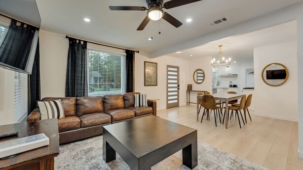 A modern living room with a brown leather sofa, a dark coffee table, and a dining area with a chandelier.