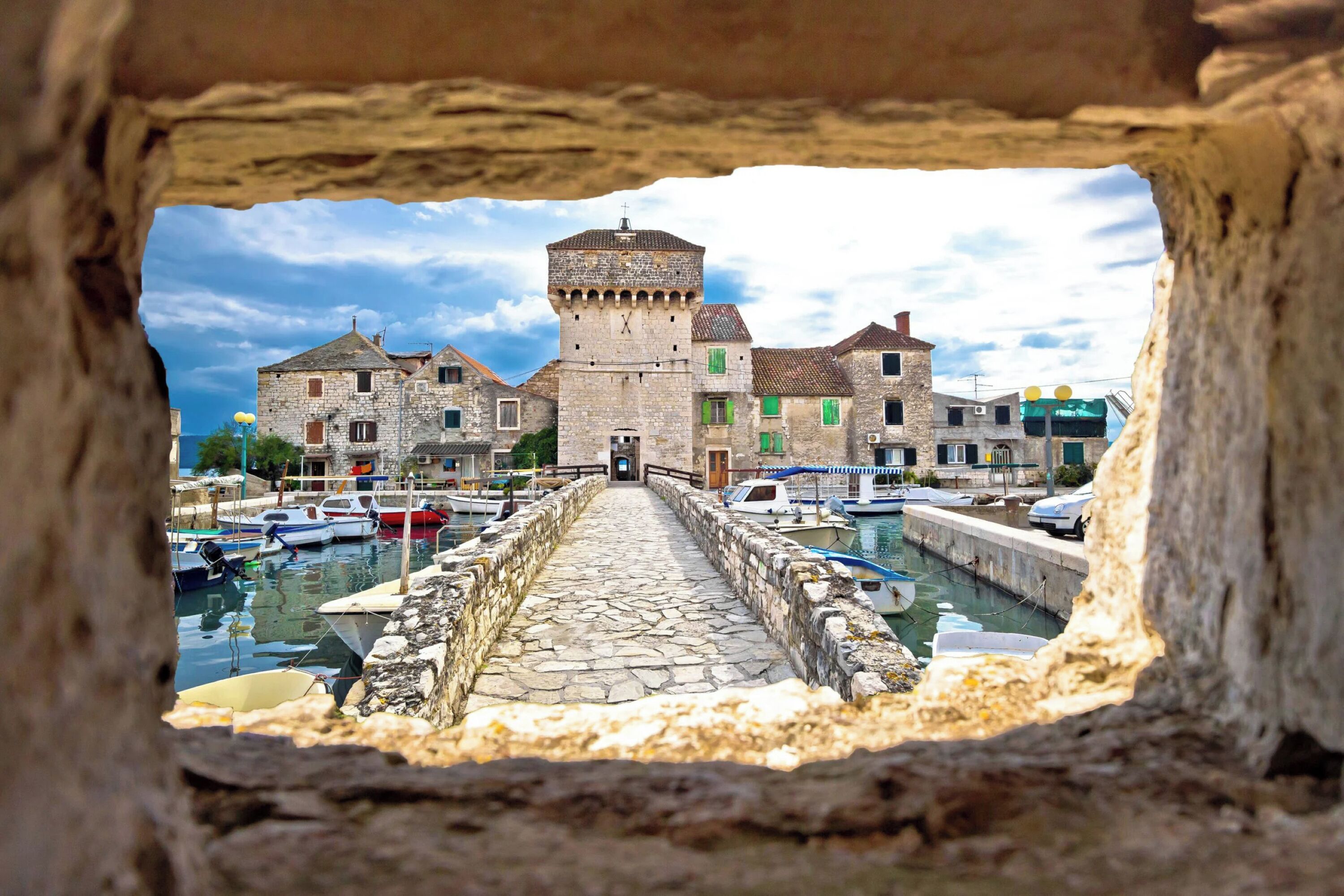 A stone bridge leading to a historic town with a prominent tower and traditional buildings.