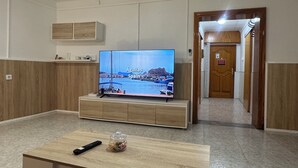 Une chambre d’hôtel avec un téléviseur posé sur un meuble en bois, une télécommande et un petit vase décoratif sur une table en bois.